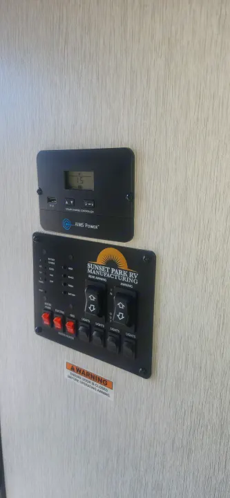 RV rental's interior control panel: monitoring battery/tanks, managing water, lights, and awnings, with solar charger display.. Sunset Park RV Sun Lite 2024