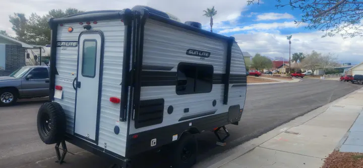 Sun Lite Sport travel trailer (SunsetTrailers.com), an ideal RV rental, parked with jacks on a residential street.. Sunset Park RV Sun Lite 2024