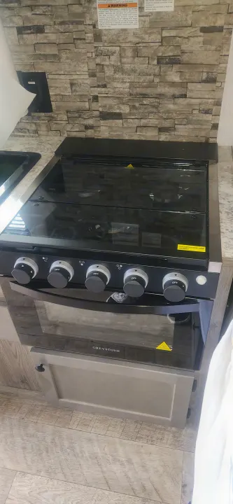 This RV rental kitchen features a compact Greystone gas stove and oven with a glass cooktop cover, ideal for cooking on the road.. Sunset Park RV Sun Lite 2024
