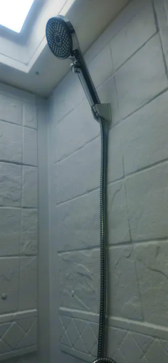Compact shower in an RV rental, featuring a modern shower head, hose, and white textured walls.. Sunset Park RV Sun Lite 2024