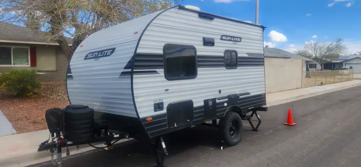 A grey Sun Lite Sport travel trailer with off-road tires, suitable for RV rental, is parked on a residential street.. Sunset Park RV Sun Lite 2024