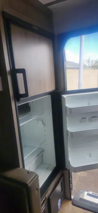 Open Dometic refrigerator inside an RV rental, displaying empty shelves, ideal for your next trip.. Sunset Park RV Sun Lite 2024