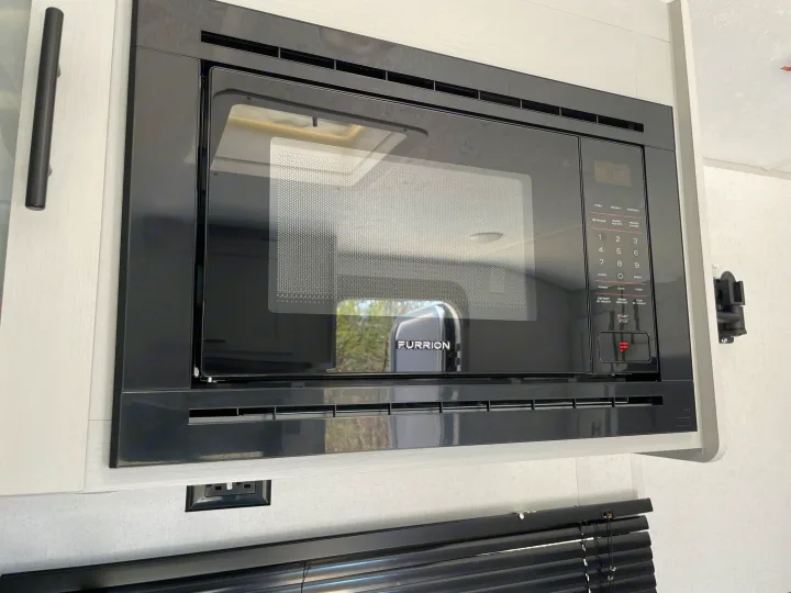 A sleek black Furrion microwave oven, typical in an RV rental, is built into the light wood cabinetry.. Forest River Salem FSX PLATINUM 2021