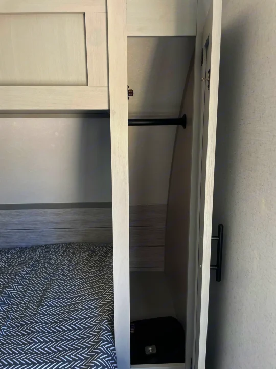 A functional RV rental bedroom: close-up of a compact closet with a hanging rod, next to a bed with patterned bedding.. Forest River Salem FSX PLATINUM 2021