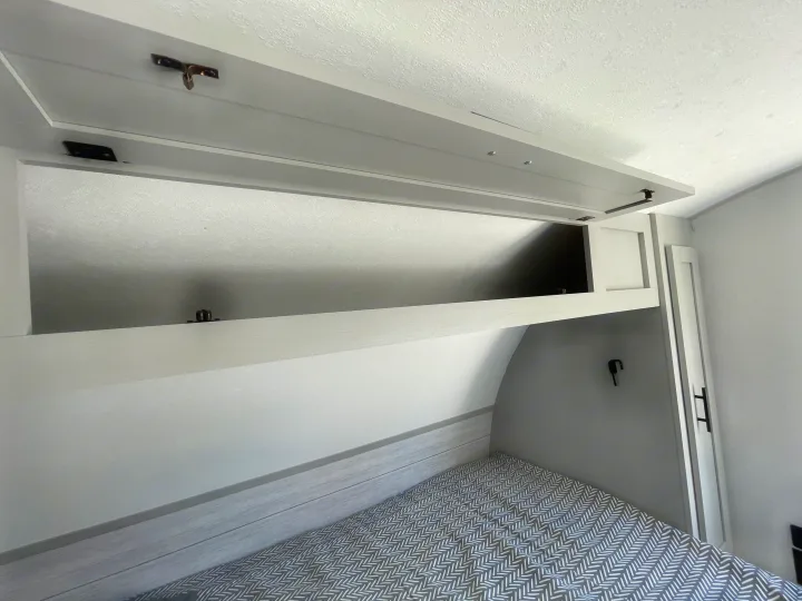 Modern RV rental bedroom showcasing open overhead storage, a patterned bed, and efficient built-in cabinets for travel.. Forest River Salem FSX PLATINUM 2021