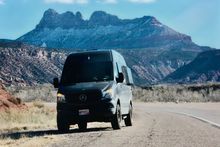 An RV rental - a dark Mercedes Sprinter van - parked on a scenic road with majestic snow-capped mountains in the background.. Mercedes Sprinter 2016