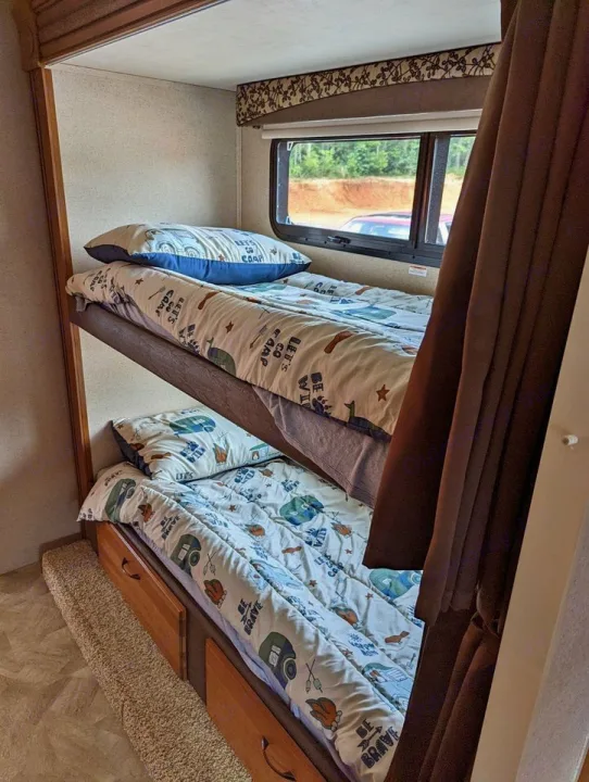 Cozy RV rental bunk beds with adventure-themed bedding, featuring a window view and under-bed storage, perfect for family camping.. Jayco Redhawk 2015