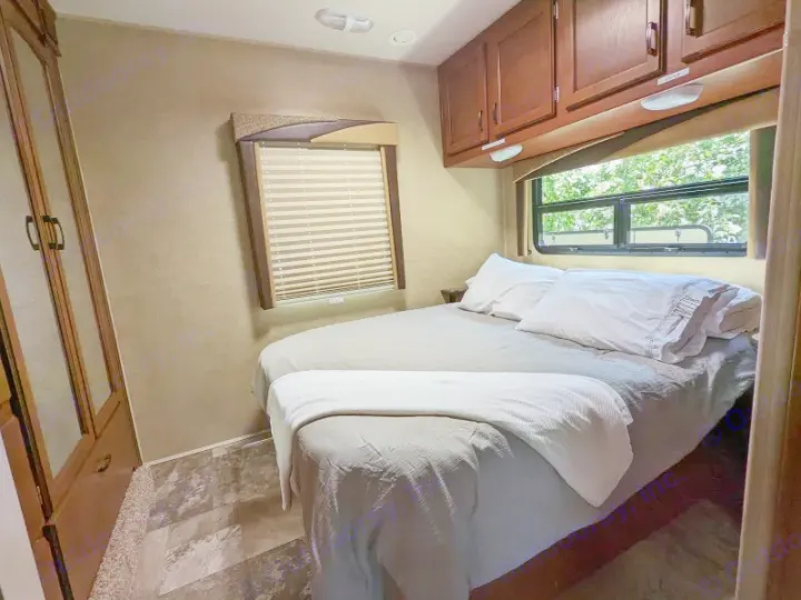 This RV rental bedroom features a comfortable bed, overhead cabinets, wardrobe, and windows, ideal for a pleasant stay.. Jayco Redhawk 2015
