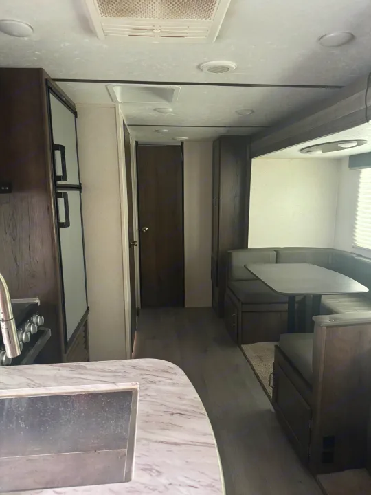 Modern RV rental interior with a functional kitchen, comfortable dining booth, and a clear hallway layout.. Keystone RV Passport SL 2021