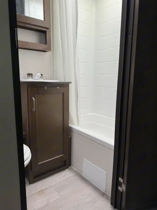 A compact RV rental bathroom is seen, featuring a vanity, sink, medicine cabinet, shower/tub, and a partial view of the toilet.. Keystone RV Passport SL 2021