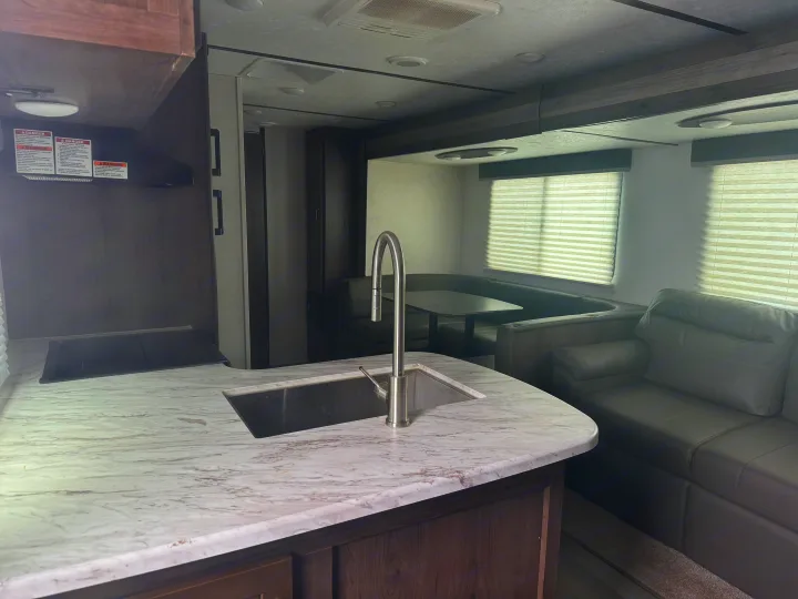 Inside a spacious RV rental: kitchen with sink, dinette, and comfy lounge. Ideal camper interior.. Keystone RV Passport SL 2021