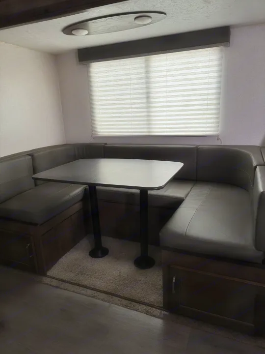 This cozy RV rental dining nook features a U-shaped booth with storage, a table, and a window with blinds.. Keystone RV Passport SL 2021