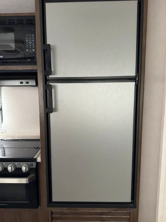 Essential kitchen appliances in an RV rental: a sleek silver fridge, microwave, and oven unit.. Keystone RV Passport SL 2021