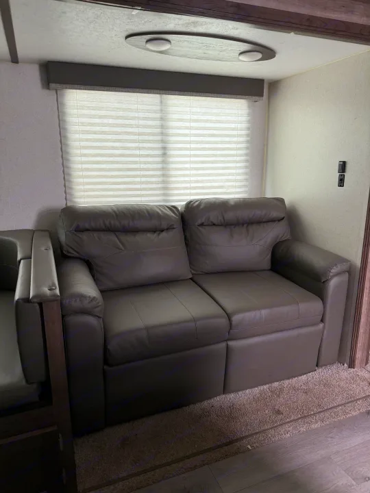 Cozy RV rental living space with plush gray recliners, a large window with blinds, and modern ceiling lights for travel comfort.. Keystone RV Passport SL 2021