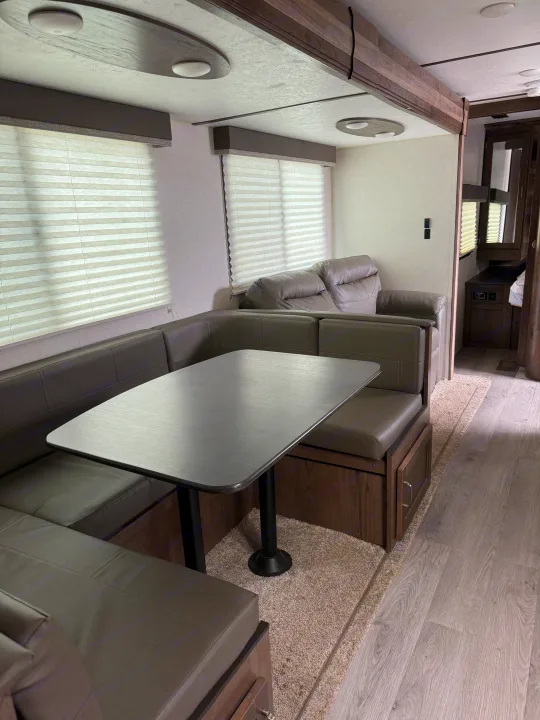 Inside a clean rv rental: spacious dinette with gray seating, sofa, and wood flooring. Bright, inviting living area.. Keystone RV Passport SL 2021