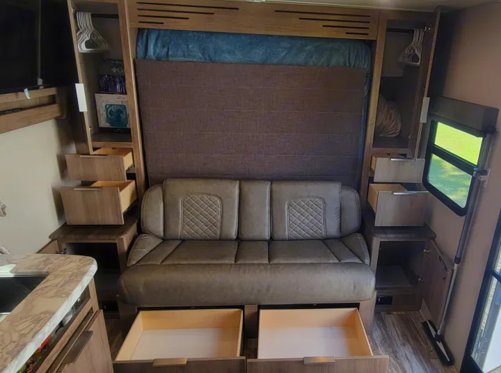 An RV rental's clever interior: a sofa convertible to a bed, open drawers, and storage cabinets. Perfect for efficient living.. Grand Design Imagine XLS 2021