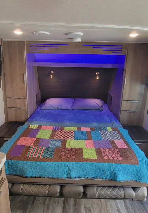 RV rental bedroom: cozy bed with colorful quilt, ample storage, and blue accent lighting for a comfortable stay.. Grand Design Imagine XLS 2021