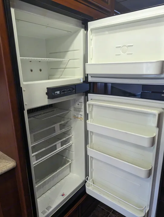 Open Norcold refrigerator in an rv rental, showing empty interior, wire shelves, and freezer compartment.. Thor Other 2014