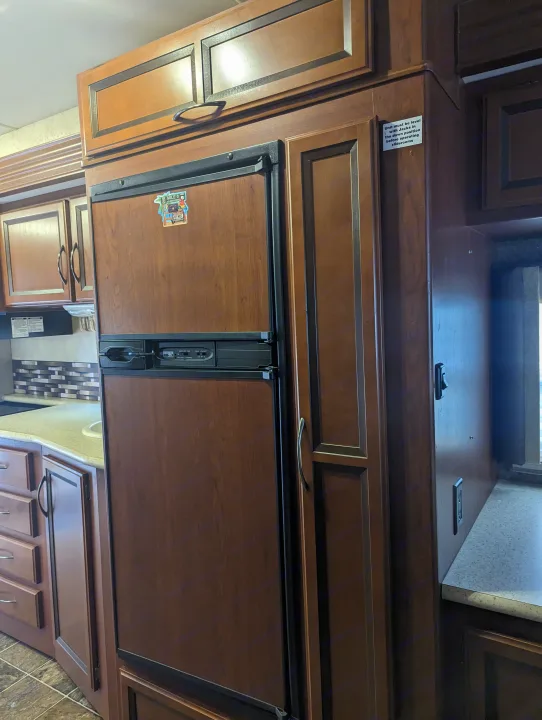 An RV rental kitchen featuring dark wood cabinets, a built-in refrigerator, a countertop, and a sink for mobile living.. Thor Other 2014