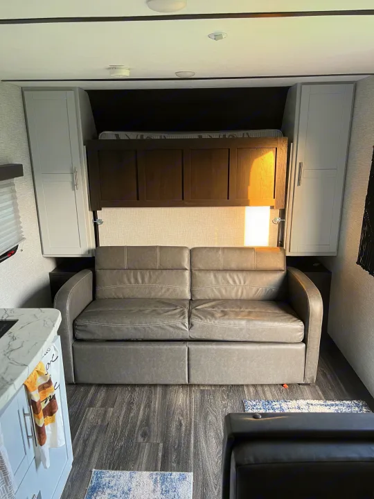 Modern RV rental living area with a versatile sofa bed, overhead cabinets, and wood-look flooring.. Keystone RV Bullet Crossfire 2021