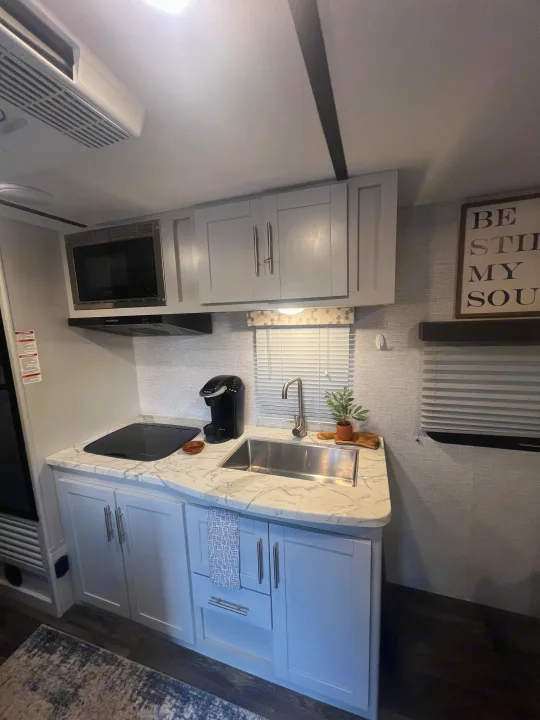 Bright RV rental kitchen with light gray cabinets, marble-look countertops, modern appliances & a large sink.. Keystone RV Bullet Crossfire 2021