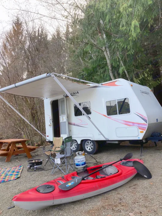 Enjoy nature with this RV rental setup: travel trailer, red kayak, & picnic table at a scenic campsite.. Takena Takena Trailer 2010