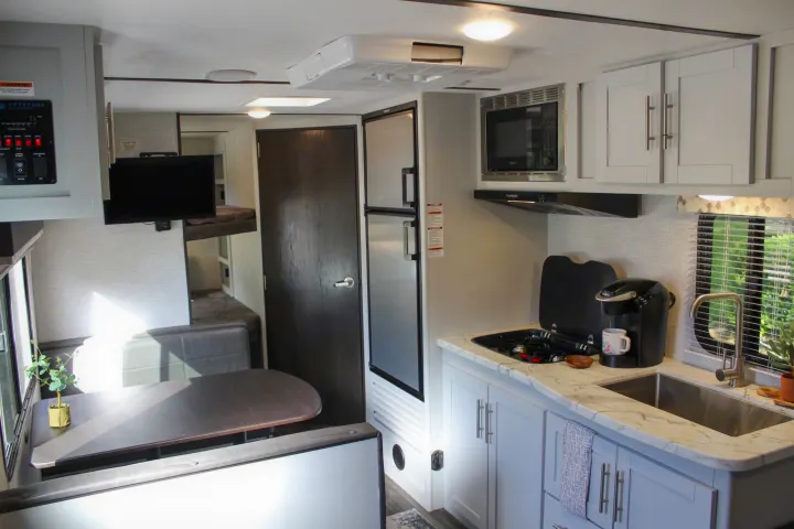 Inside an RV rental: a compact living space featuring a kitchen with sink, stove, microwave, a dinette, and bunk beds.. Keystone RV Bullet Crossfire 2021