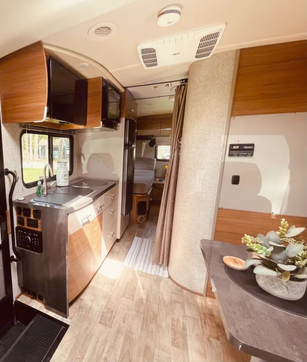 Inside an RV rental: a modern, compact living space with kitchen, dining area, rear bed, and panel controls.. Winnebago View 2016