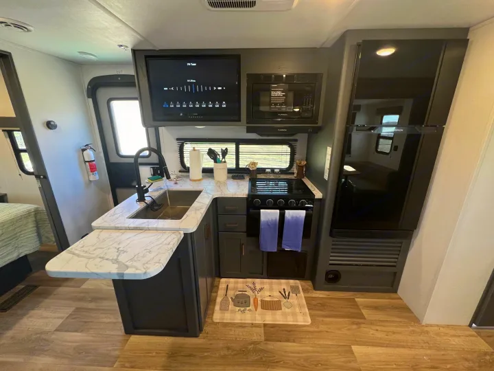 Modern rv rental kitchen with sink, stove, microwave, and fridge. Features a TV & dining counter for comfortable travel.. Keystone Bullet Crossfire 4YDTBLN25RD430760 2024