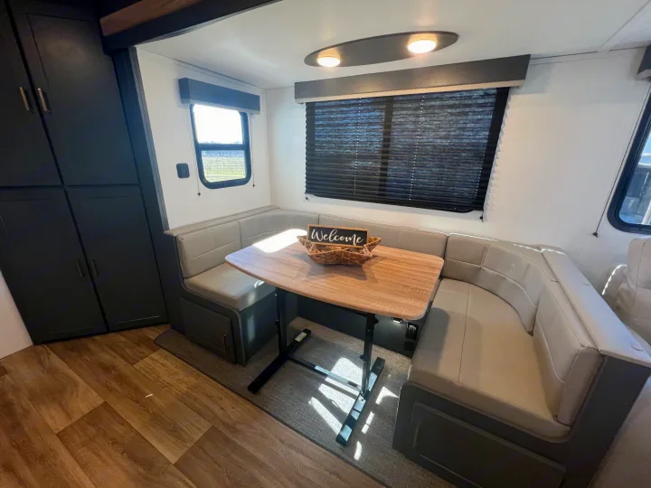 Cozy RV rental dinette featuring U-shaped bench seating, light wood table with 'Welcome' sign, dark storage cabinets, and large windows.. Keystone Bullet Crossfire 4YDTBLN25RD430760 2024