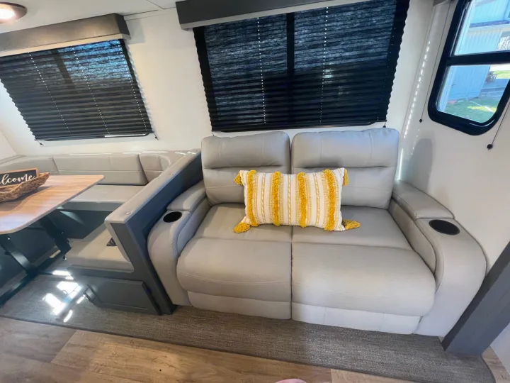 Inside a modern **rv rental**: light gray recliner sofa with cup holders, U-shaped dinette. Cozy travel living space.. Keystone Bullet Crossfire 4YDTBLN25RD430760 2024