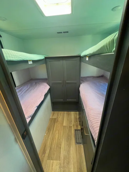 RV rental's bunk room with upper green and lower purple beds, plus a central wardrobe and drawers for storage.. Keystone Bullet Crossfire 4YDTBLN25RD430760 2024