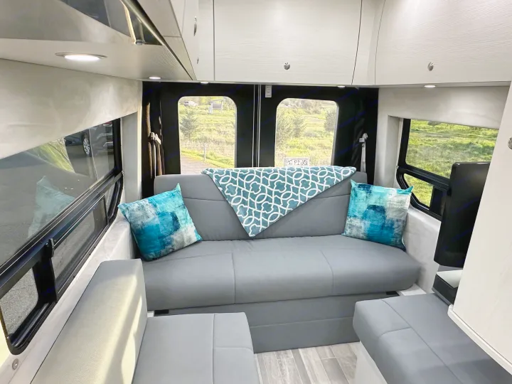 Cozy RV rental interior with a gray sofa, blue accents, and panoramic outdoor views, offering a comfortable mobile living space.. Pleasure-Way Pleasure-Way Class B 2024
