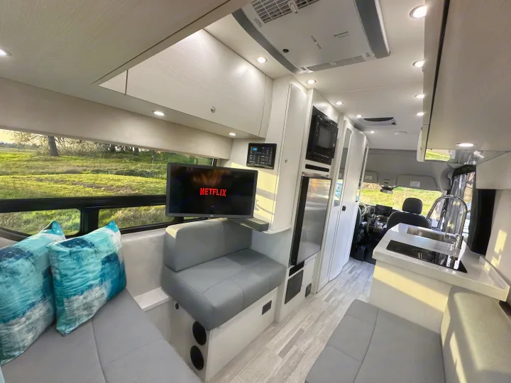 Step inside this luxurious RV rental, featuring a cozy living area with TV, modern kitchen, and scenic outdoor views.. Pleasure-Way Pleasure-Way Class B 2024