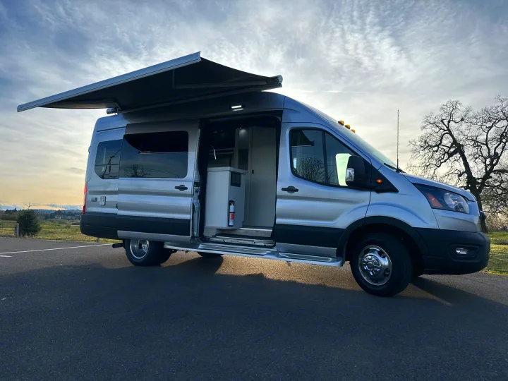 Explore this custom silver Ford Transit camper van RV rental with extended awning & visible interior.. Pleasure-Way Pleasure-Way Class B 2024