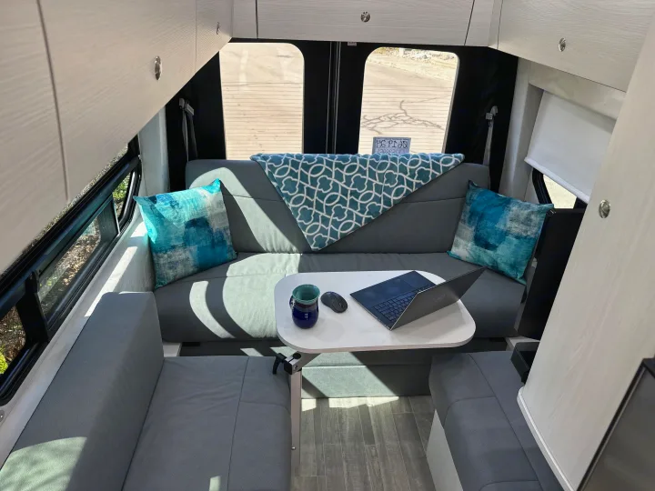 Cozy RV rental interior with grey seating, a white table with a laptop, and overhead cabinets, ideal for a mobile workspace.. Pleasure-Way Pleasure-Way Class B 2024