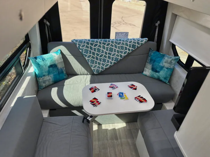 Cozy RV rental interior showing a U-shaped lounge with a table, UNO game cards, and blue pillows.. Pleasure-Way Pleasure-Way Class B 2024