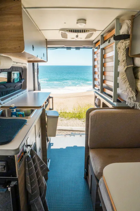 Inside an RV rental, enjoy ocean views from the back. Features a kitchen, seating area, and cozy mobile living space.. Winnebago Solis Pocket 2022