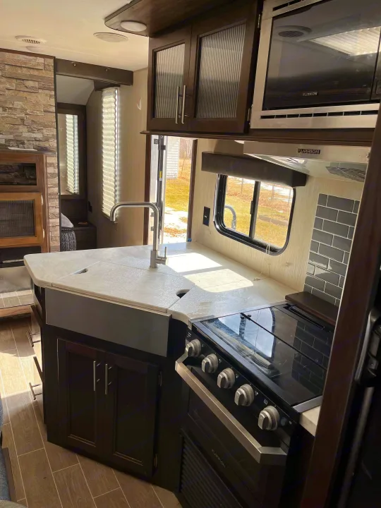Spacious RV rental kitchen: modern design with a farmhouse sink, black stove, microwave, and dark cabinets.. Forest River Cherokee Grey Wolf 2020