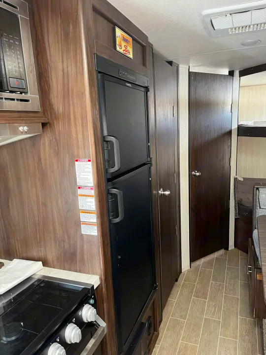 Inside this RV rental's kitchen area, you see a black refrigerator, microwave, stovetop, and bunk beds, offering a cozy camper interior.. Forest River Cherokee Grey Wolf 2020