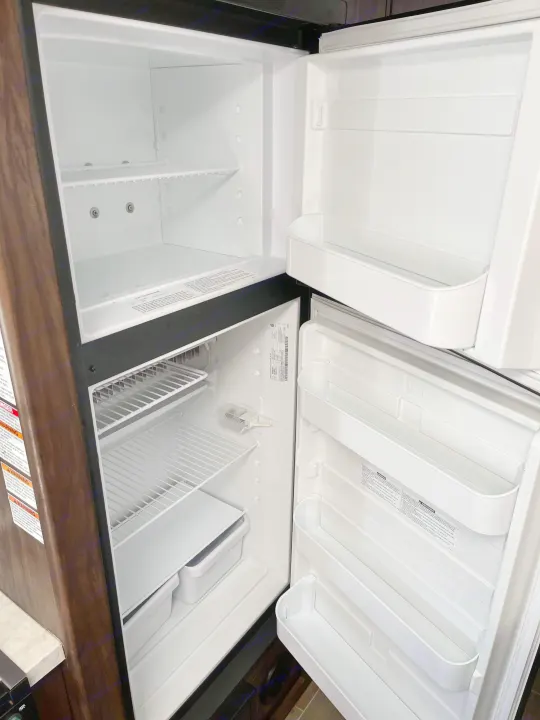 RV rental: Open, empty, and clean refrigerator, showcasing shelves and door storage. Ready for your journey's provisions.. Forest River Cherokee Grey Wolf 2020
