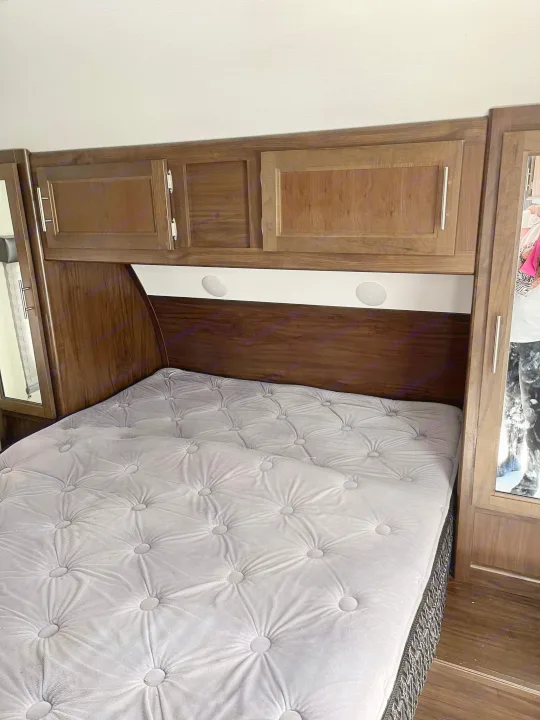 An RV rental bedroom: tufted grey bed, dark wood cabinets, and integrated lighting for a cozy interior.. Forest River Cherokee Grey Wolf 2020