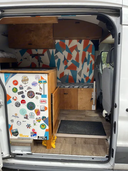 RV rental: Custom camper van interior with wood cabinetry, a colorful geometric wall, and a unique sticker collection.. Ford Transit 2015