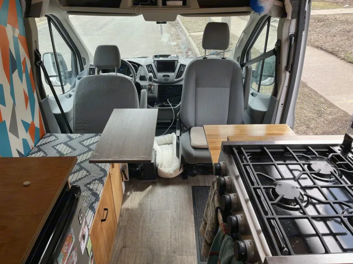 Step inside this custom RV rental: fully equipped kitchen, comfortable bench seating, and front cabin view for your van adventures.. Ford Transit 2015