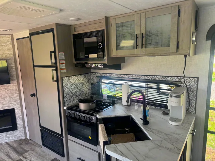 Inside a modern **rv rental** kitchen: fridge, microwave, gas range, sink, and Keurig on a marble-look counter, ready for travel.. Dutchmen Coleman Light 2023