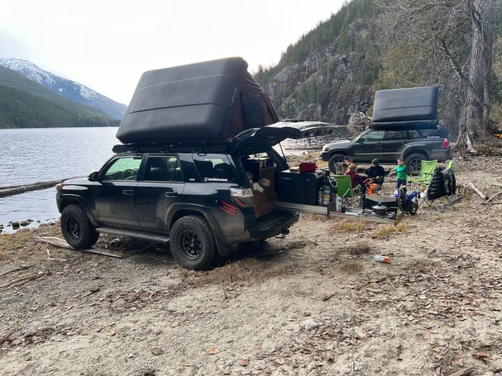 Lakeside camping with custom RV rental setups: two black SUVs, rooftop tents, open kitchen, campfire, family.. Toyota Other 2015