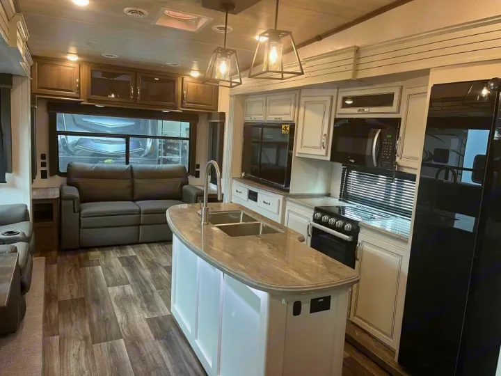 Modern RV rental interior: well-lit kitchen with island, sink, stove, fridge, plus comfortable living area with sofa.. Keystone Cougar 2022