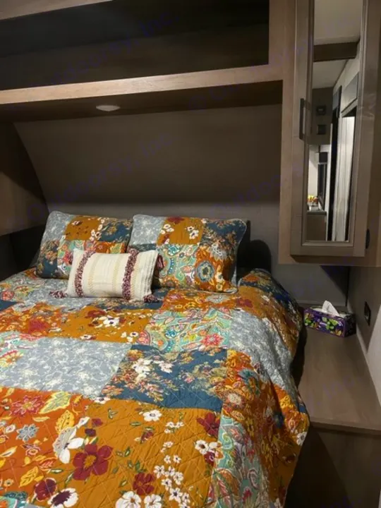 Cozy RV rental bedroom with a vibrant patchwork quilt, pillows, and built-in overhead storage.. Highland Ridge RV Open Range 2023