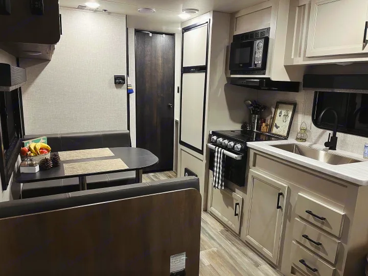 This clean RV rental interior features a kitchen with appliances, sink, and a comfortable dining booth.. Highland Ridge RV Open Range 2023