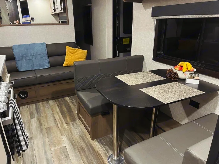 Spacious RV rental interior featuring a dark grey couch, dining booth with a table, fruit bowl, and wood-look flooring.. Highland Ridge RV Open Range 2023